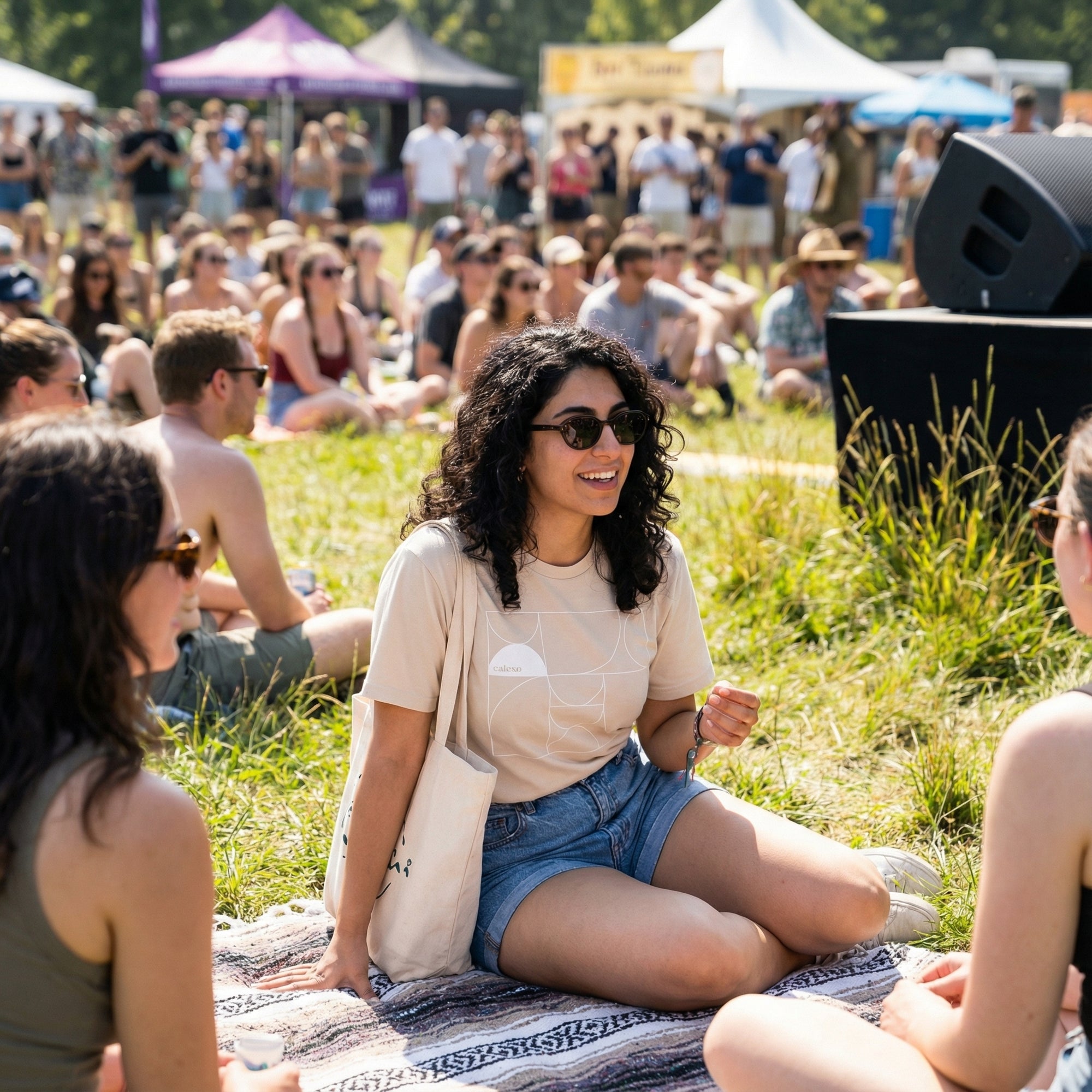 Woman sitting on a blanket at a music festival with a crowd in the background