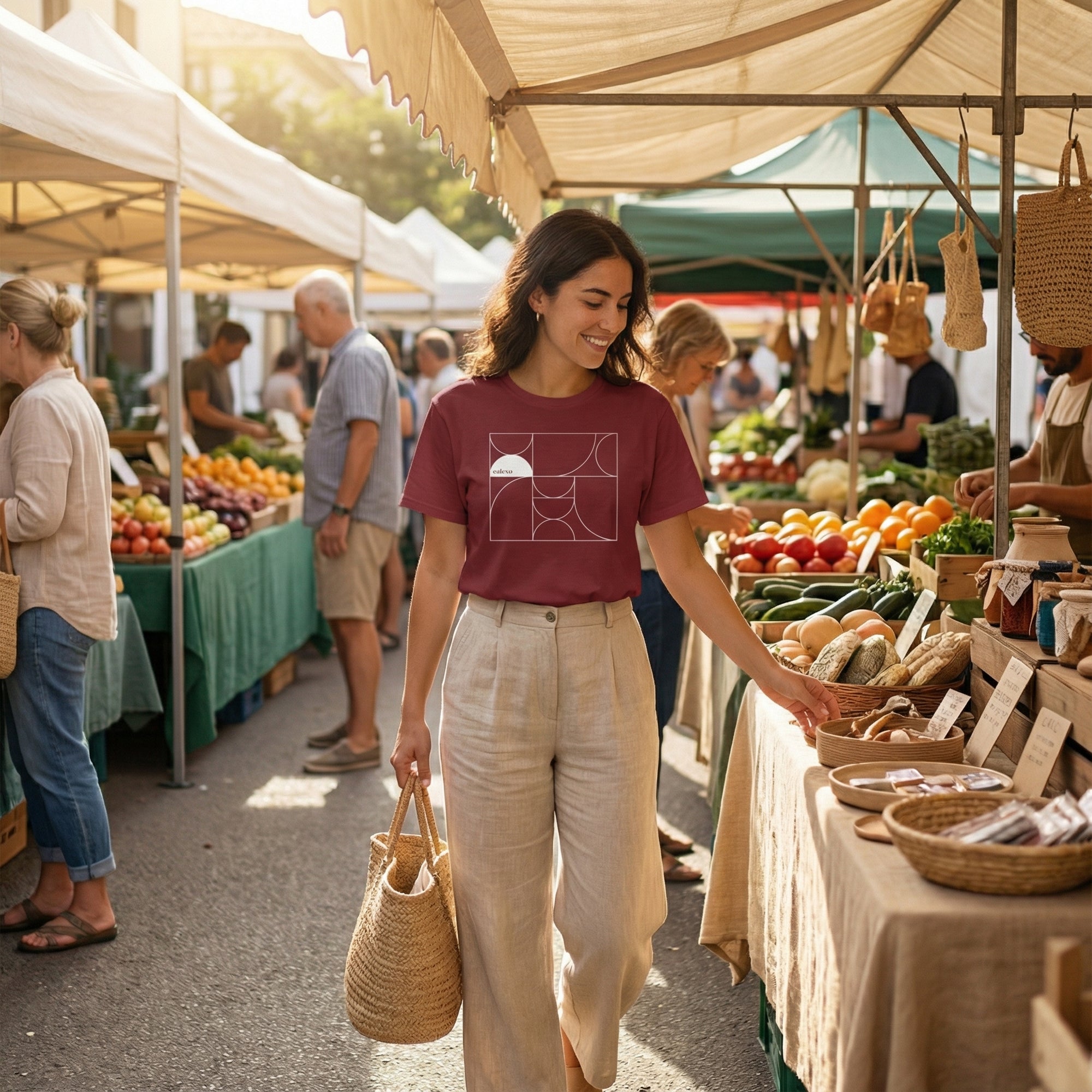 Woman shopping at an outdoor farmers market with produce tables and people in the background.