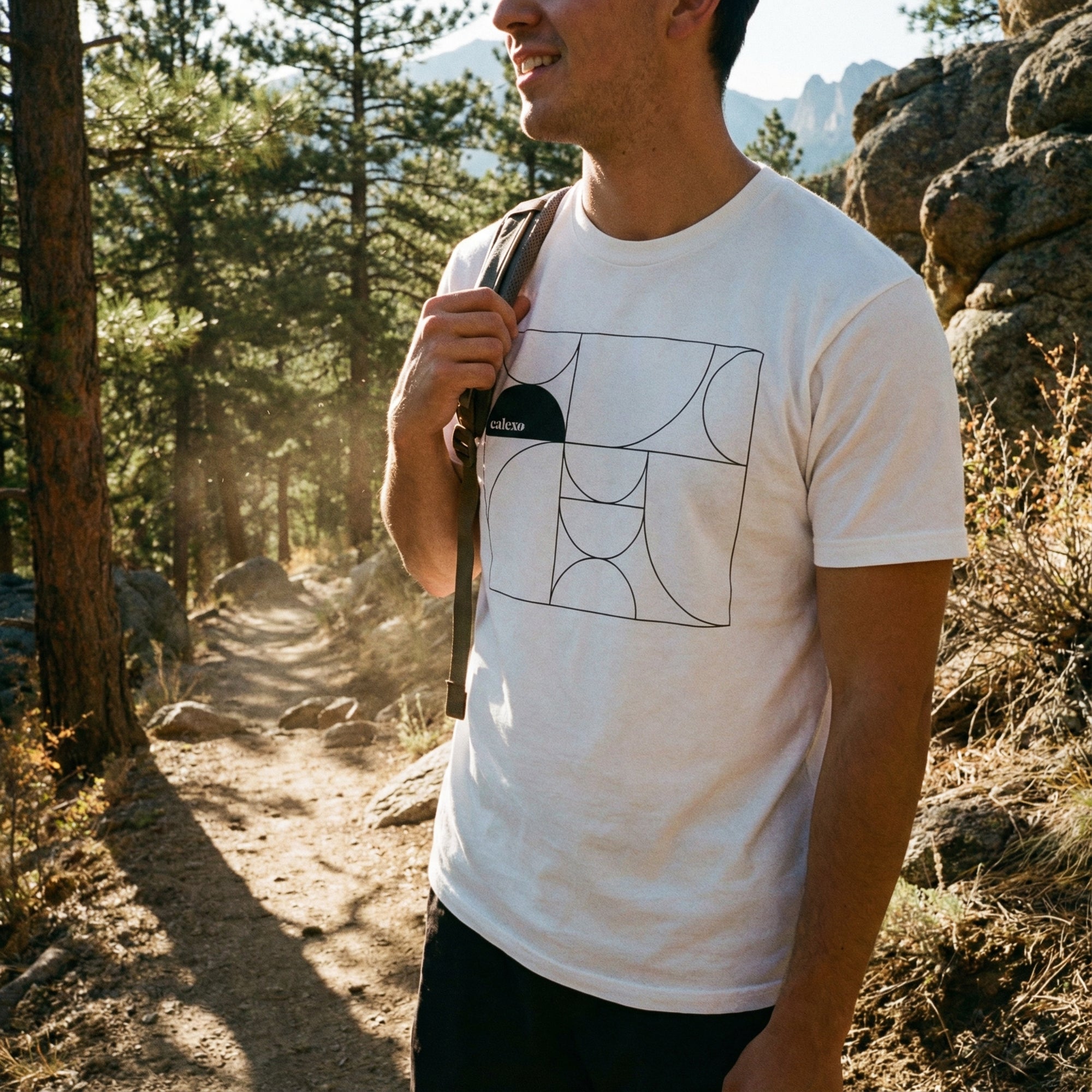 Man hiking in a forest wearing a white t-shirt with a geometric design.